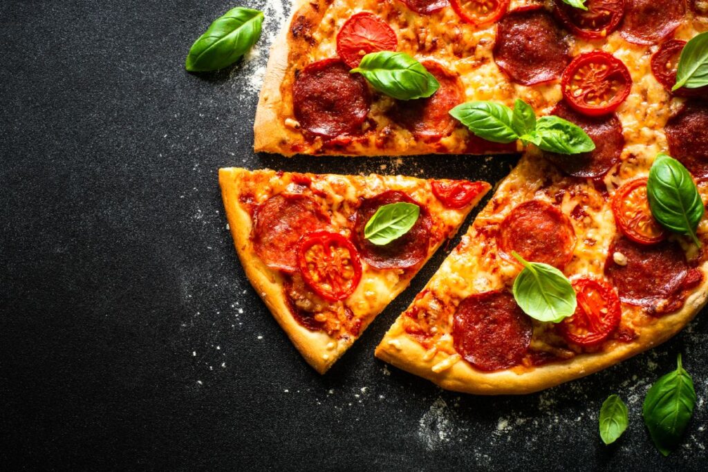 Pizza on black background. Traditional italian pizza with salami cheese, tomatoes and basil. Top view with copy space.