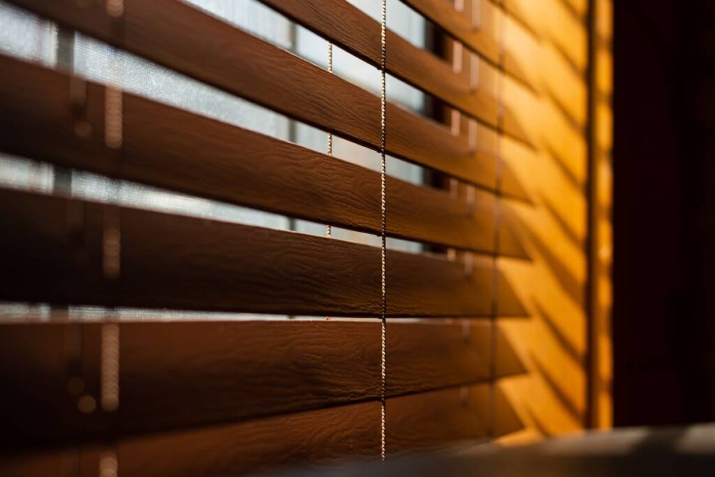 A closeup shot of wooden blinds next to a window with sunlight on the side