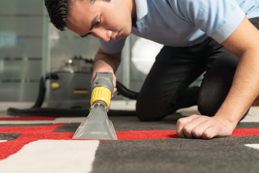 Close up of laundry worker cleaning carpet with special equipment. Young worker on his knees cleaning carpet.