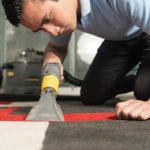 Close up of laundry worker cleaning carpet with special equipment. Young worker on his knees cleaning carpet.