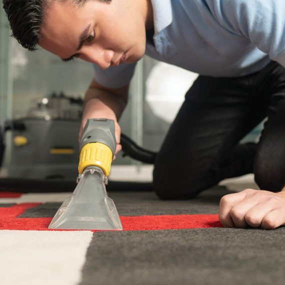 Close up of laundry worker cleaning carpet with special equipment. Young worker on his knees cleaning carpet.