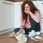 Young caucasian woman having eating disorder and eating greedily on the floor