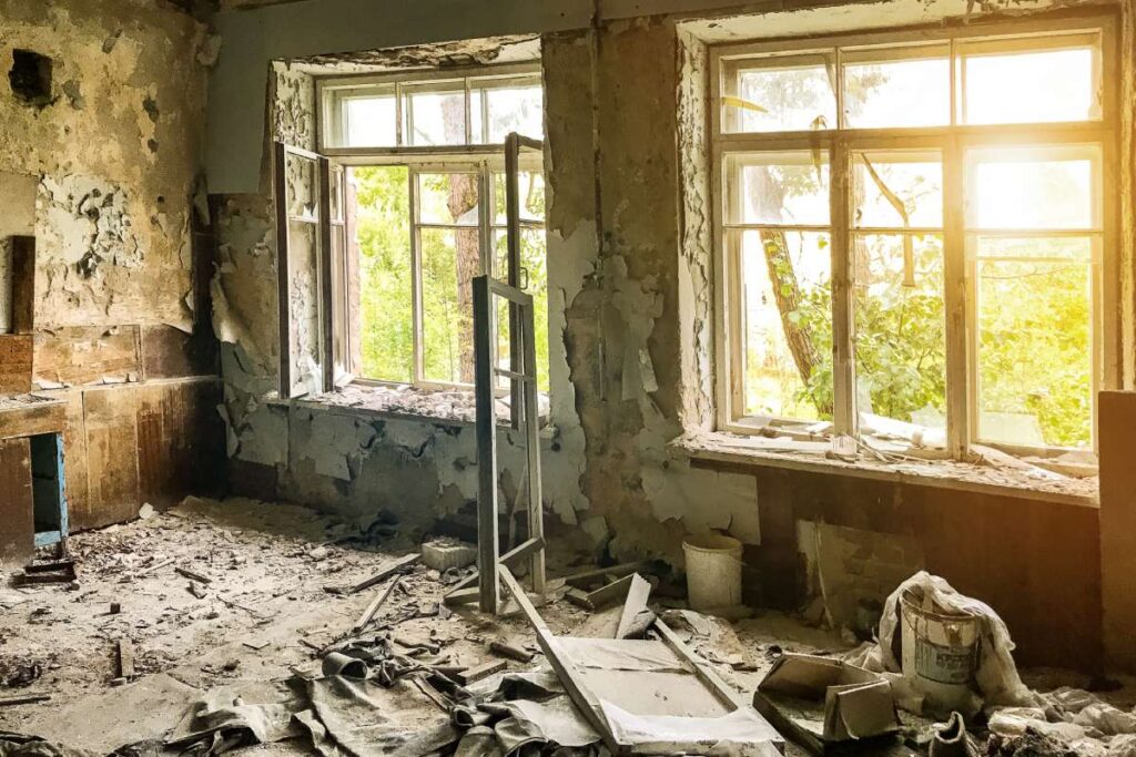 An abandoned Soviet military barracks in a military unit. Empty grunge abandoned ruined room with shabby walls and sunlight from large windows. Grungy warehouse basement background. Copy text space