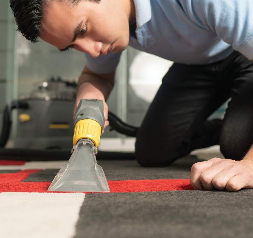 Close up of laundry worker cleaning carpet with special equipment. Young worker on his knees cleaning carpet.