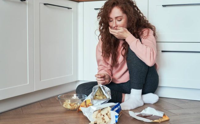 Young caucasian woman having eating disorder and eating greedily on the floor