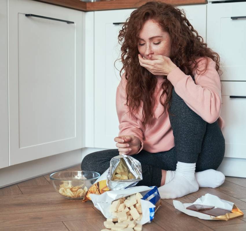 Young caucasian woman having eating disorder and eating greedily on the floor